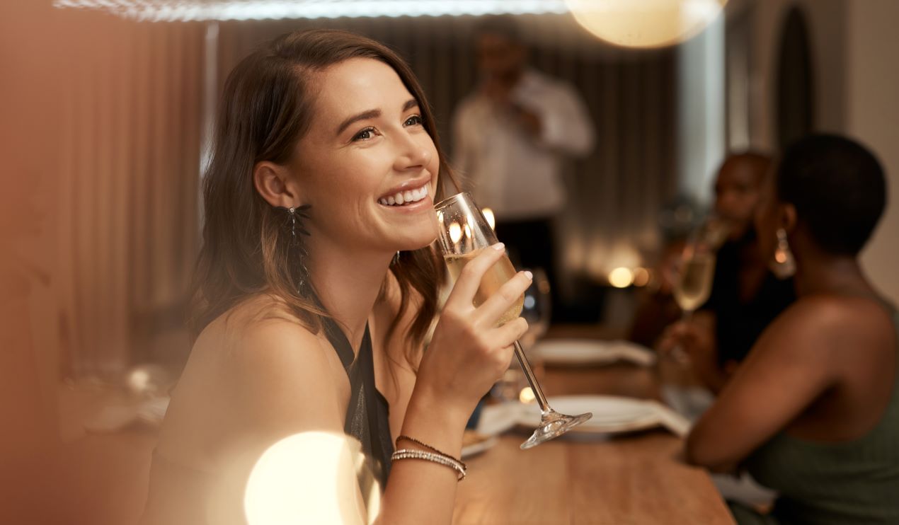 Frau mit Champagnerglas lächelt bei einem stilvollen Dinner – Symbol für Luxus und Eleganz im Escort Service Berlin